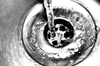 Water pouring into a metal sink drain, creating ripples and bubbles