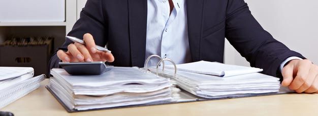 A man in a suit is sitting at a desk using a calculator.