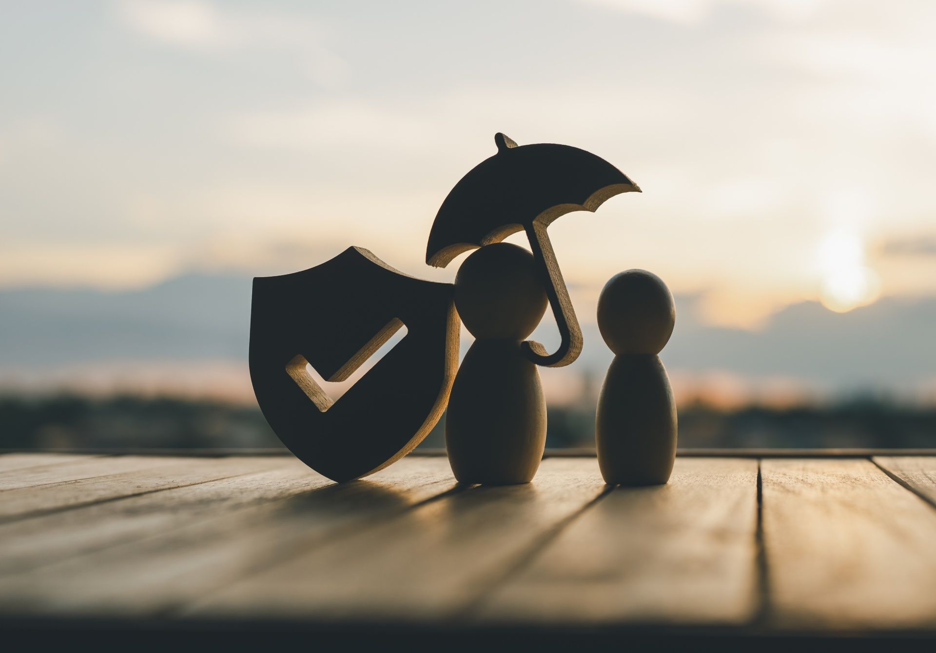 A wooden figure holding an umbrella next to a check mark and a shield on a wooden table.