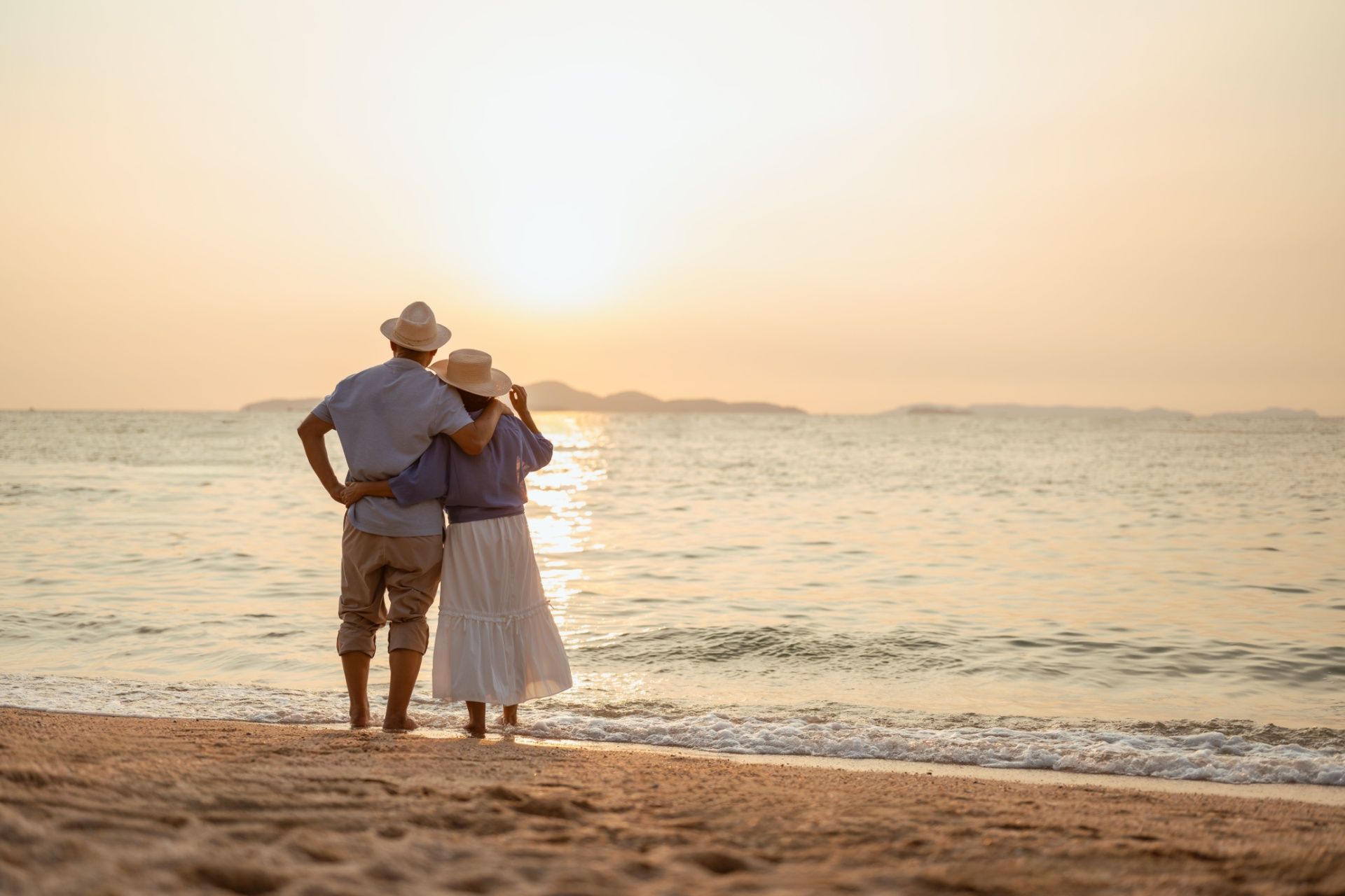 Couple on beach, embracing, watching sunset over ocean.