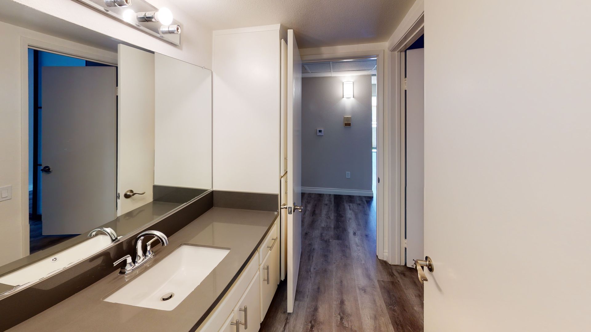 Bathroom with long countertop, mirror, and a hallway with wood flooring.