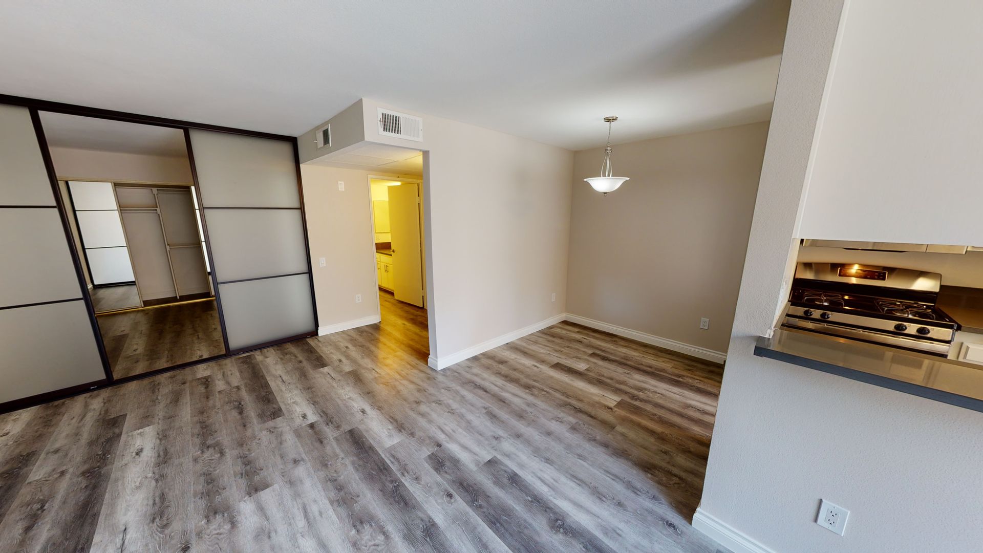 Interior view of a living space with sliding mirrored doors, wood flooring, and a dining area.