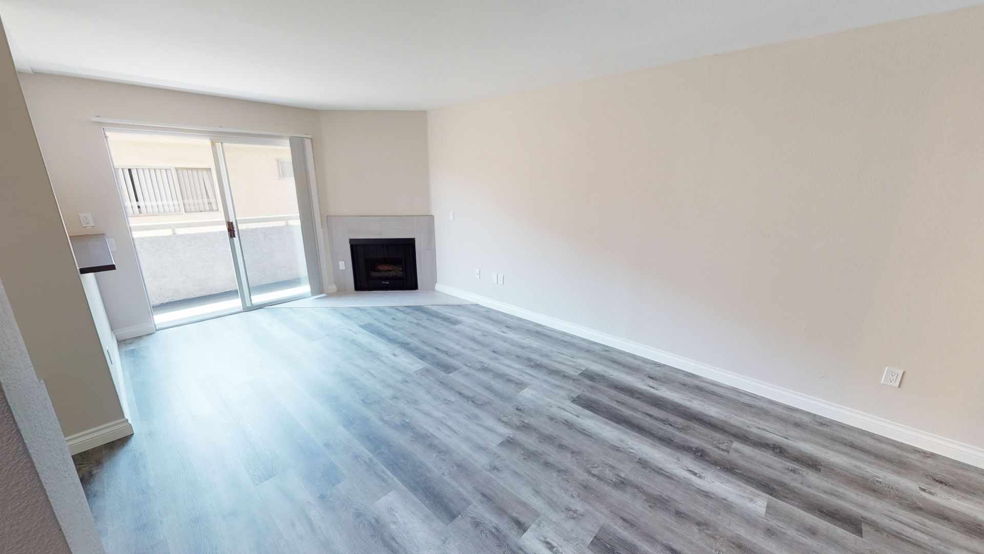 Empty living room with gray wood-look flooring, fireplace, and sliding door to balcony.