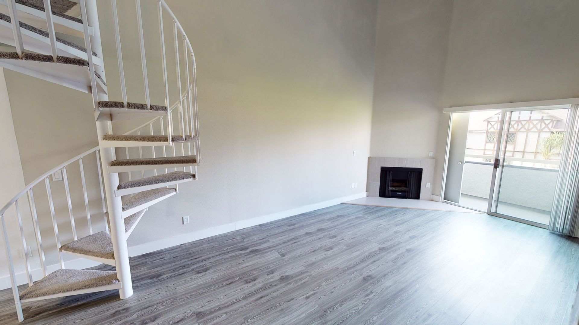 Empty living room with spiral staircase, fireplace, and sliding glass door to balcony.