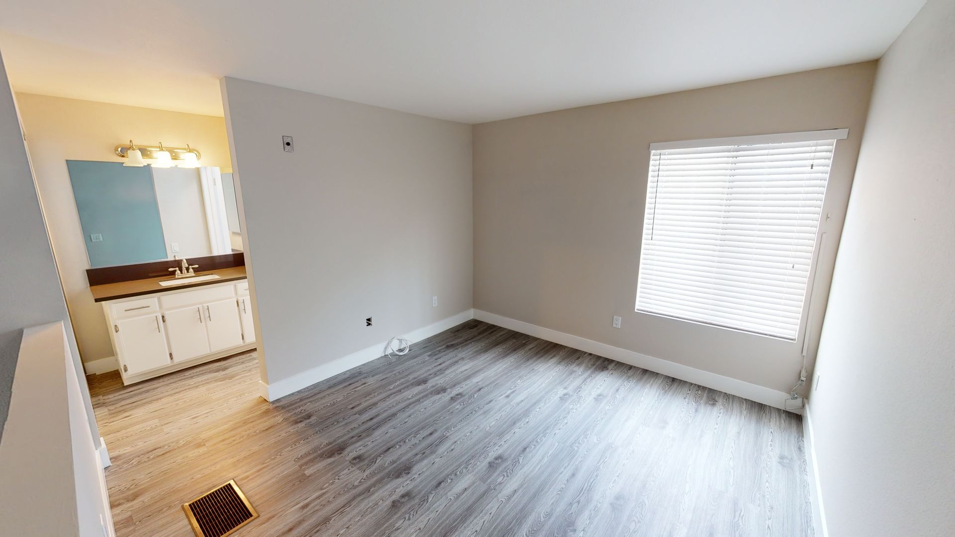 Empty room with gray flooring, a window with blinds, and a doorway to a bathroom.