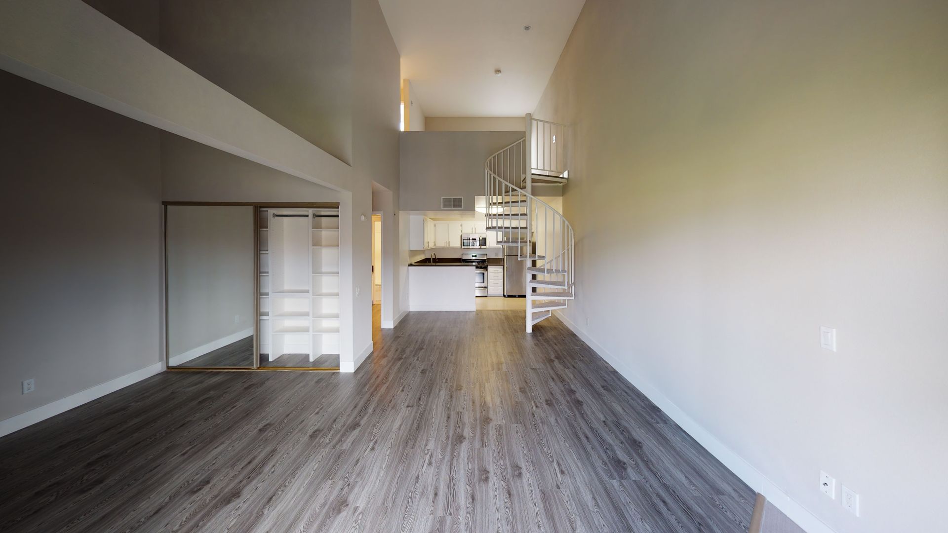 Interior view of a modern loft apartment with spiral staircase, high ceilings, and light gray walls.