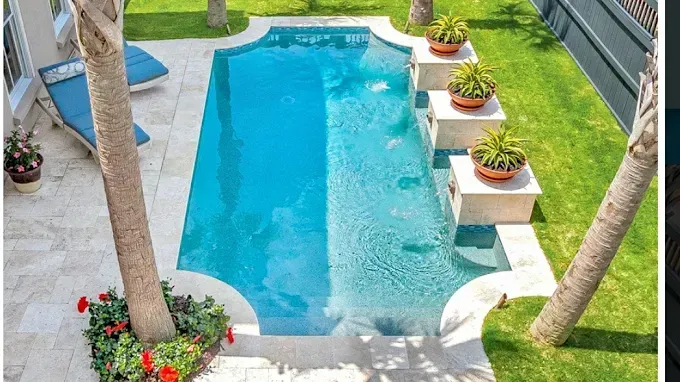 A large swimming pool in the backyard of a house surrounded by palm trees.