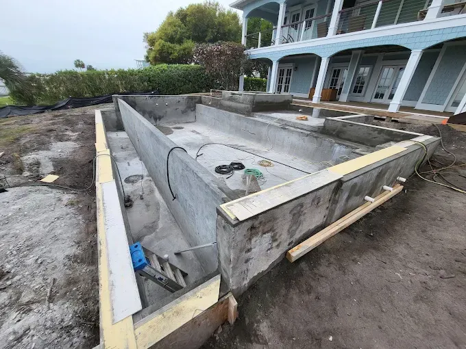 A large concrete pool is being built in front of a large house.