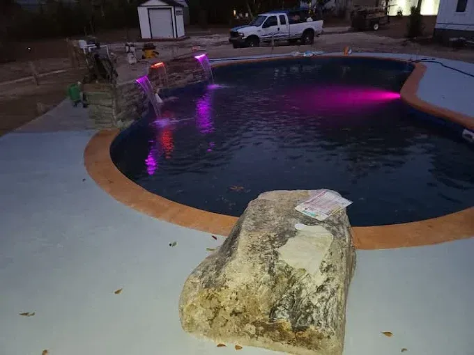 A large rock is sitting next to a large swimming pool.