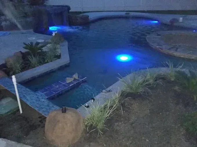 A swimming pool is lit up at night with blue lights.