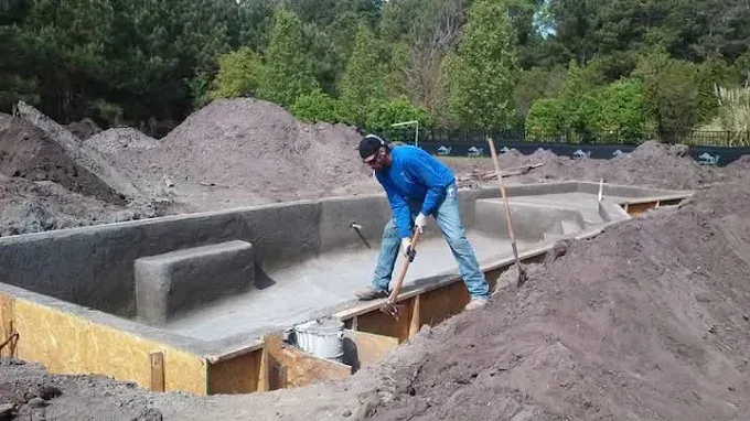 A man is standing in a pile of dirt next to a pool.