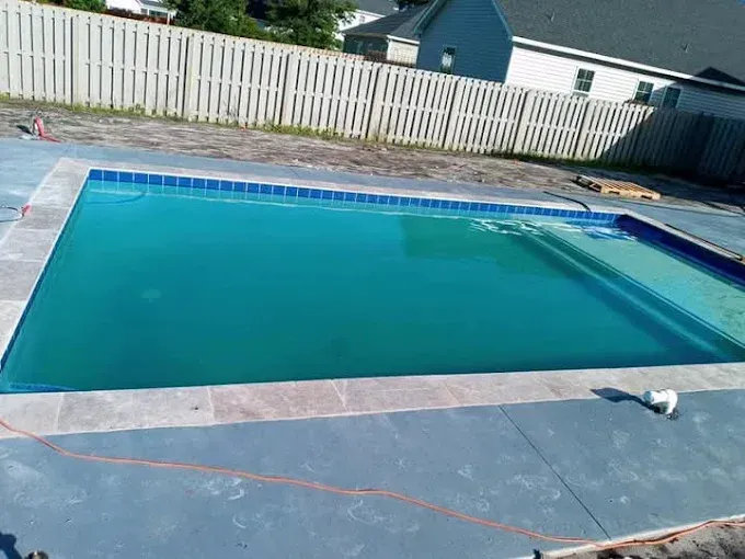 A large swimming pool with a fence in the background and a house in the background.