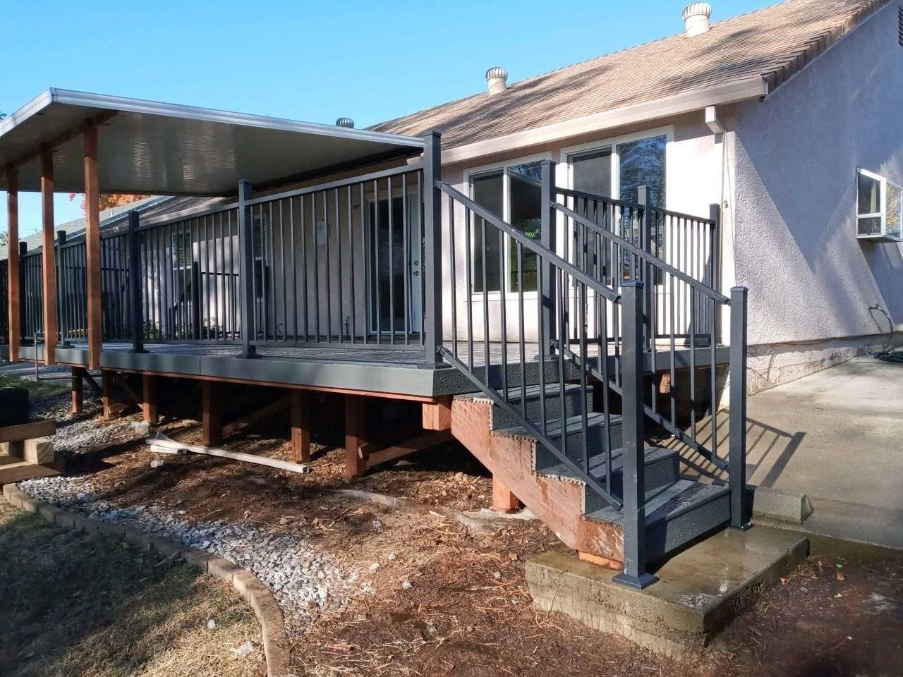 A modern deck with dark gray railings and stairs, a covered patio area, and a light-colored house exterior in the background.