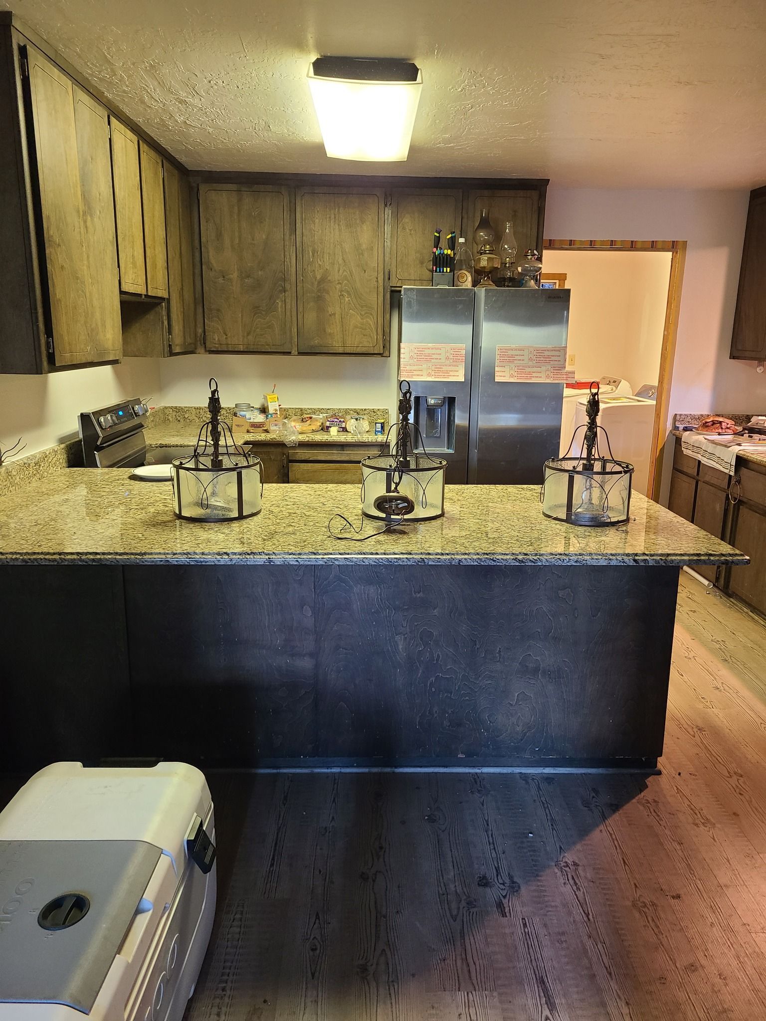 A kitchen with dark wood cabinets, a speckled granite countertop, three small appliances, and a stainless steel fridge.