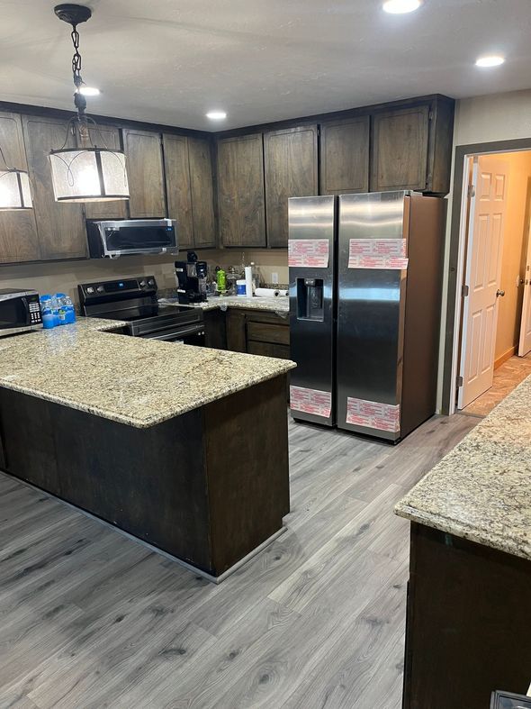 Kitchen with dark cabinets, granite countertops, an island, and a stainless steel side-by-side refrigerator.