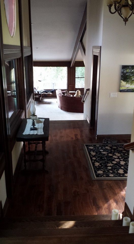A view from the top of a staircase looking down into a home's entryway toward a living room with large windows.