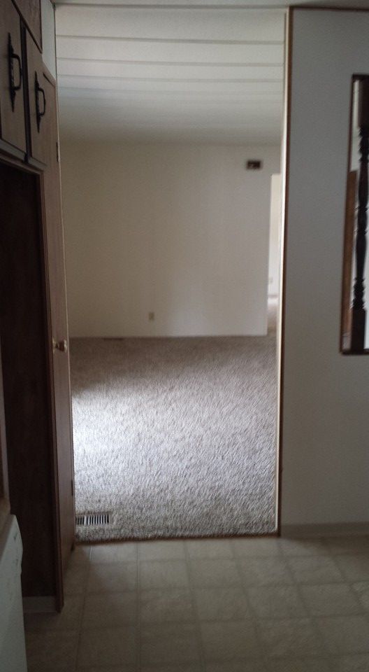 A view from a tiled entryway looking through a doorway into an empty living room with light-colored carpet and walls.