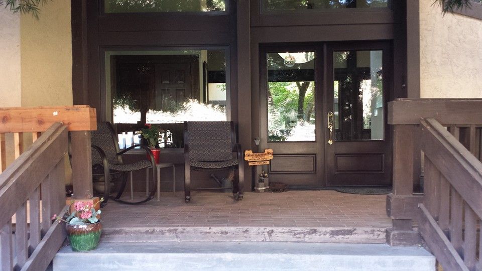 A dark brown double door entrance with a stone porch, two rocking chairs, and a small sign hanging near the door.