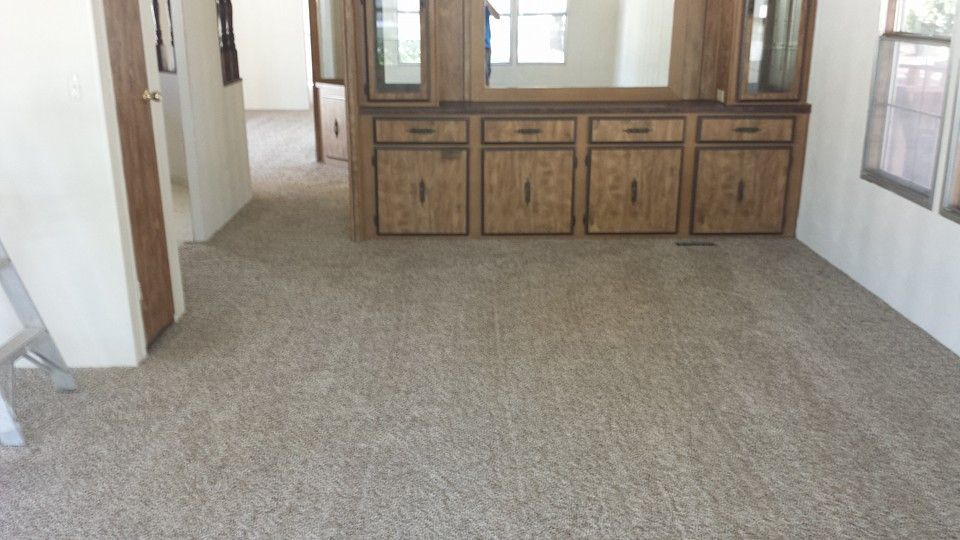 A beige-carpeted room with a wooden built-in cabinet featuring four drawers and cabinets below a mirror.