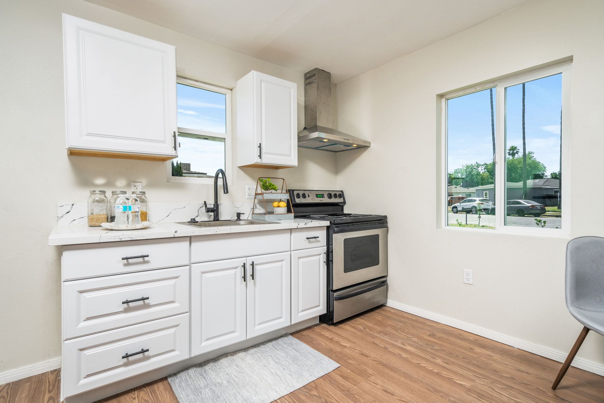 A modern kitchen with white cabinets, stainless steel appliances, a range hood, a window, and wood-look flooring.