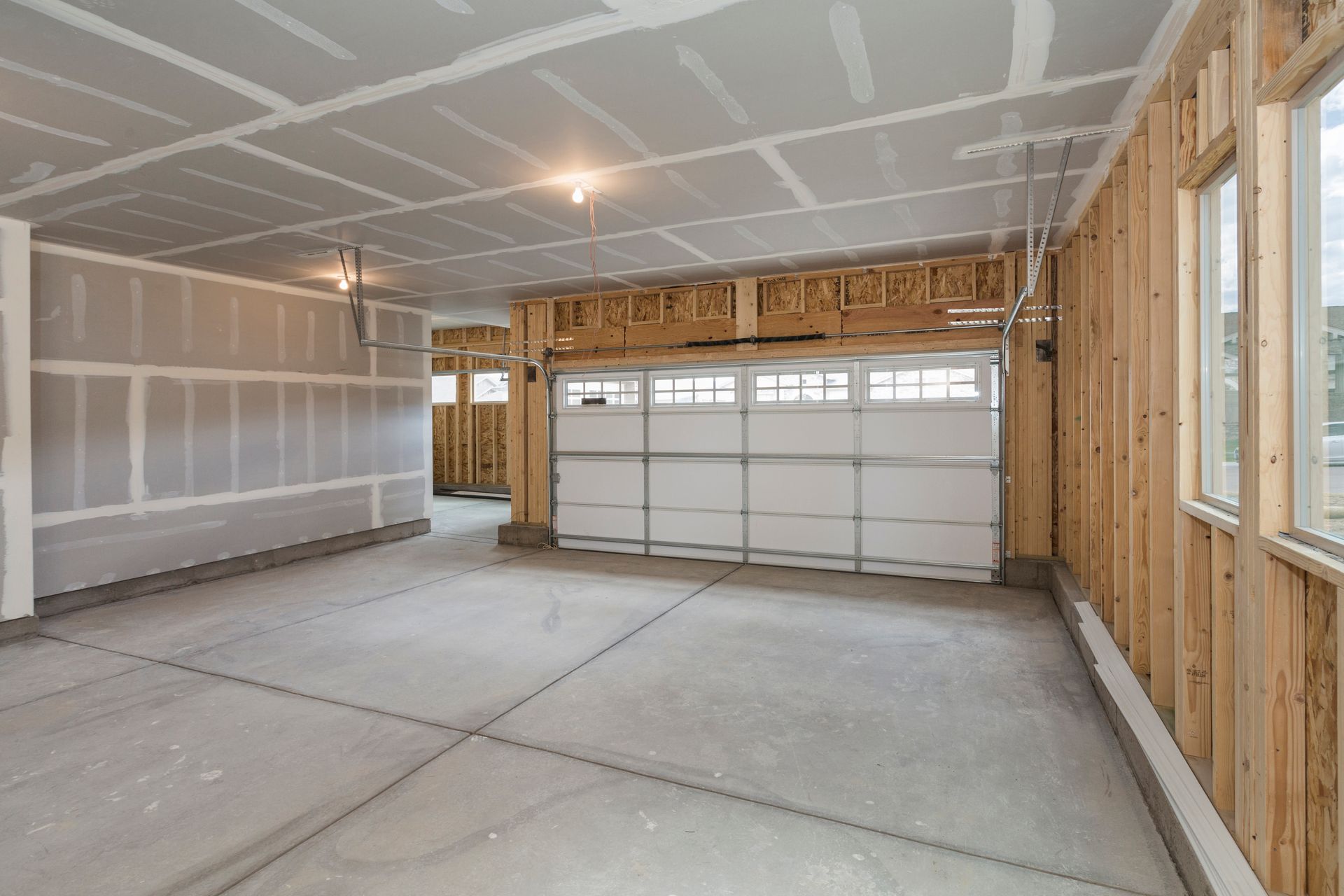An unfinished three-car garage interior with drywall ceilings, concrete floors, and visible wood wall framing.