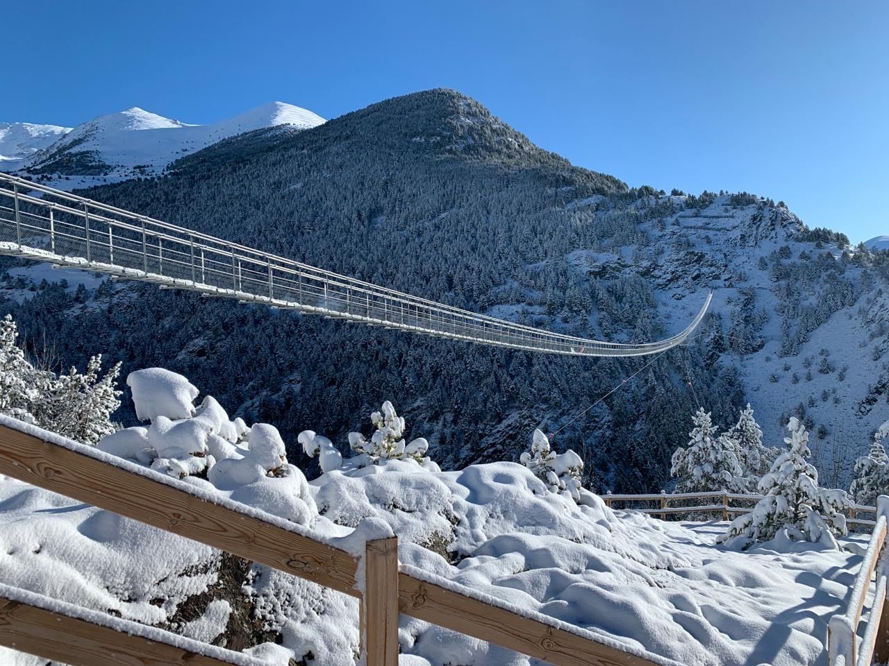 Un puente colgante sobre un valle nevado con montañas al fondo. montañas andorra valle naturaleza