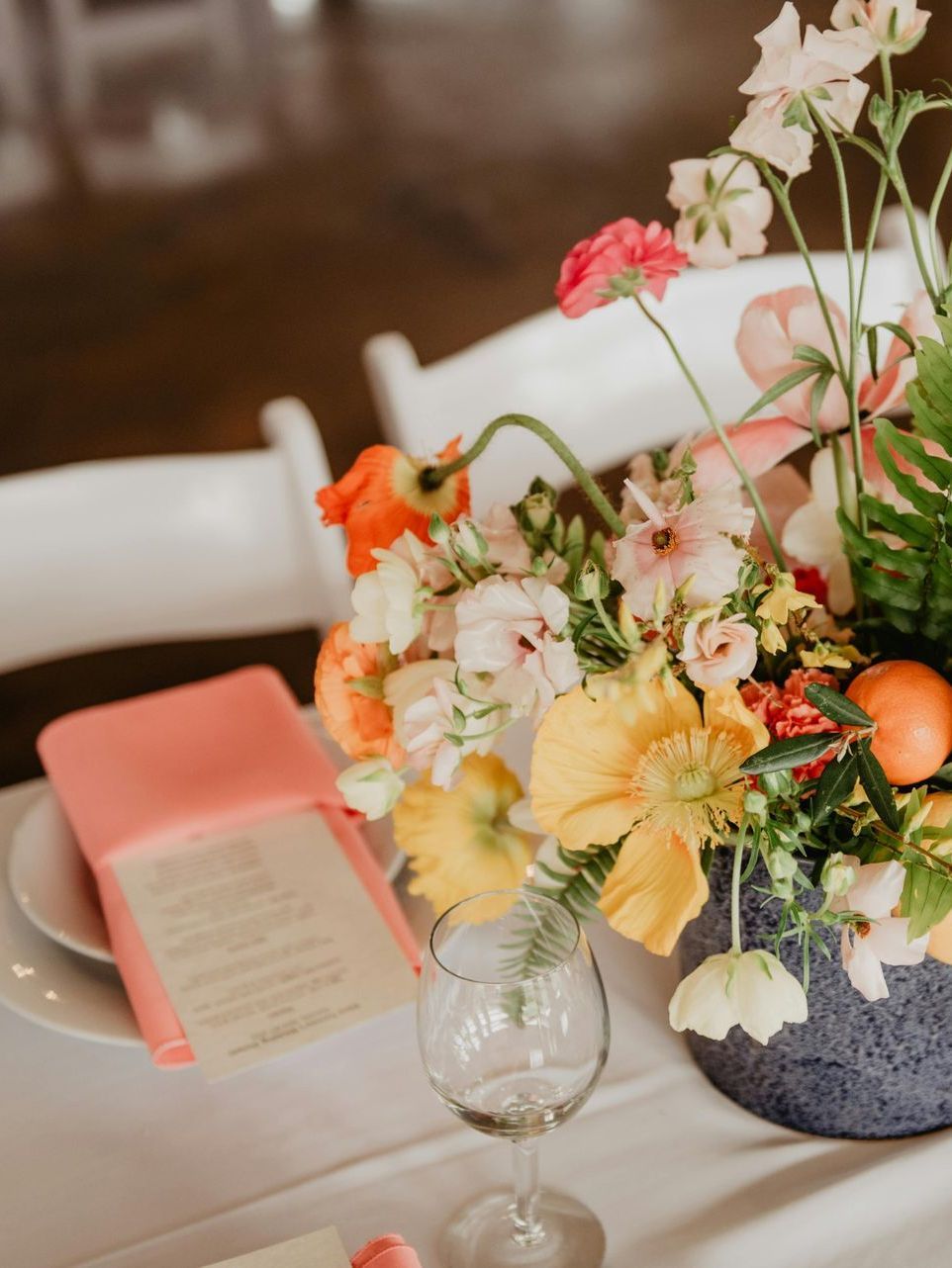 Una mesa con un jarrón de flores y una copa de vino encima.