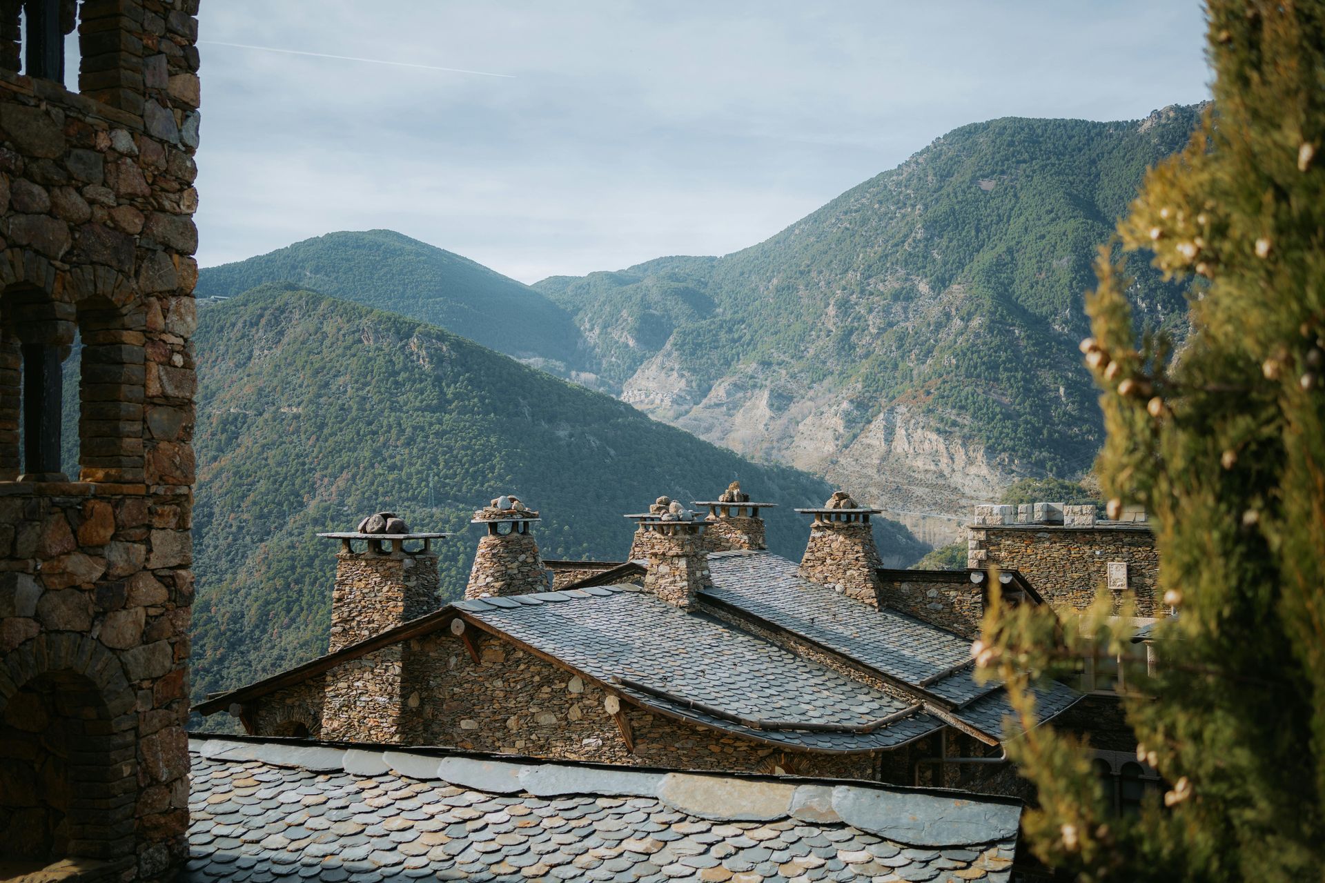 Un edificio de piedra con chimeneas en el tejado está rodeado de montañas de andorra. Naturaleza