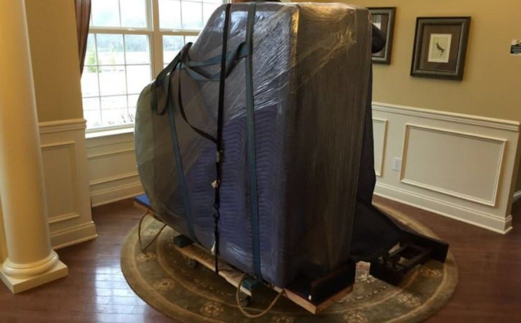 Large wrapped object on a dolly in a wood-paneled room with windows and framed wall art