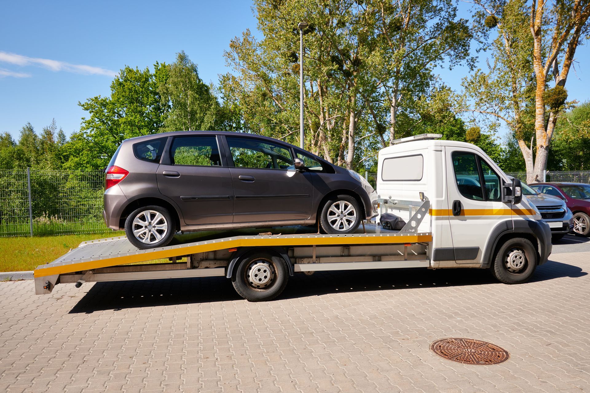 Car loaded on a flatbed tow truck parked outdoors beside trees.