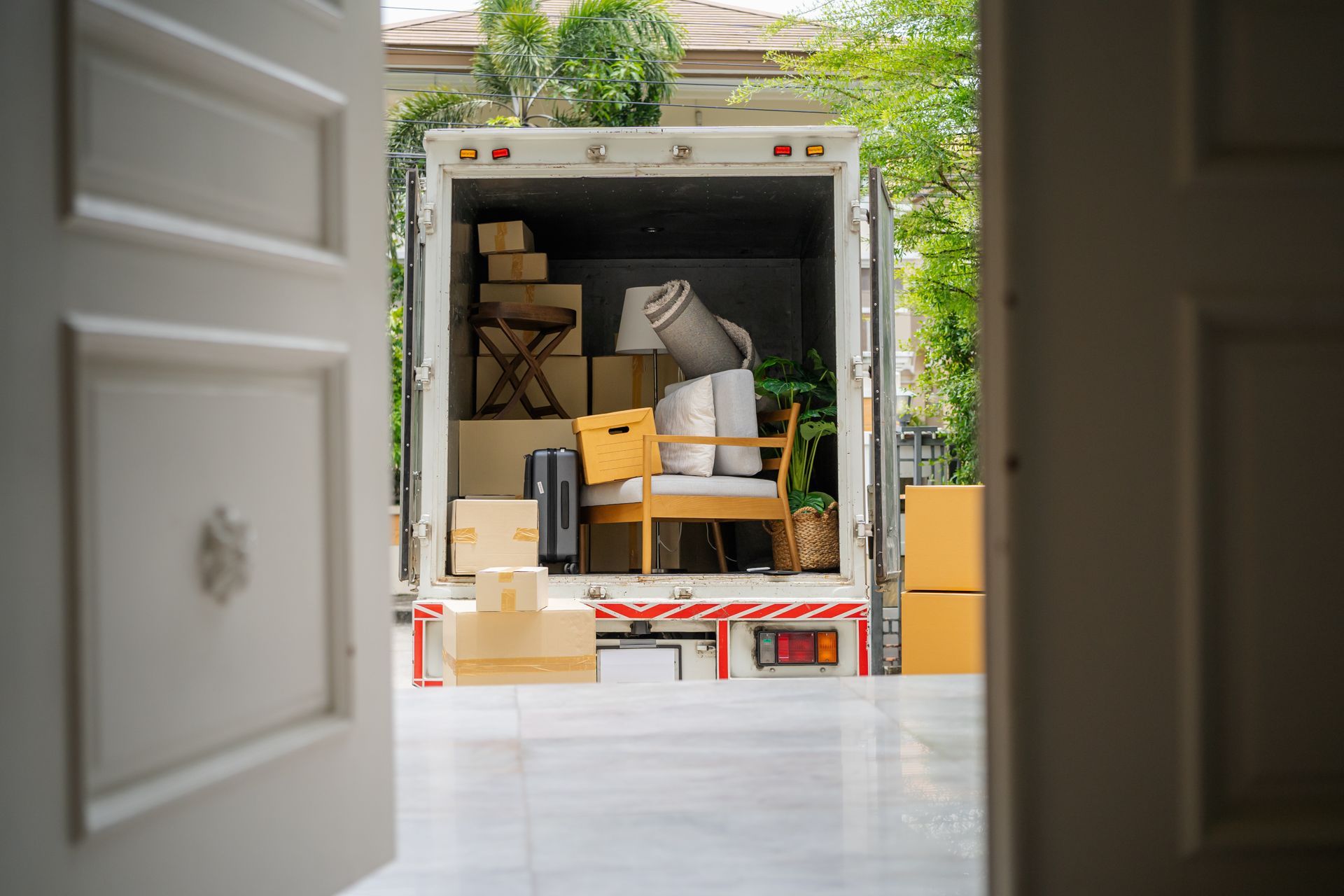 Moving truck loaded with boxes and furniture, viewed through an open doorway.