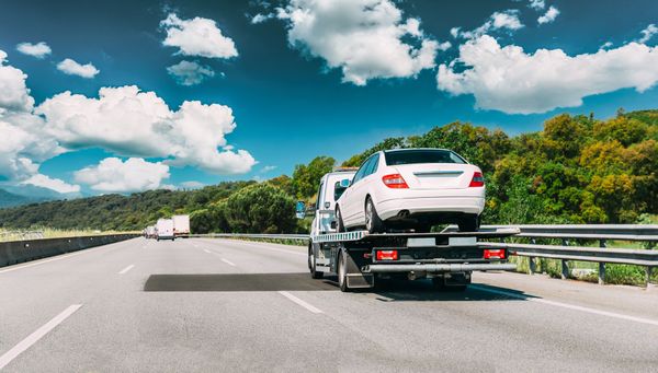 White SUV on a tow truck driving on a highway under a bright blue sky