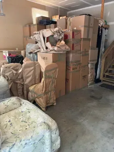 Mover wrapping furniture with protective plastic in a room with boxes and a ladder