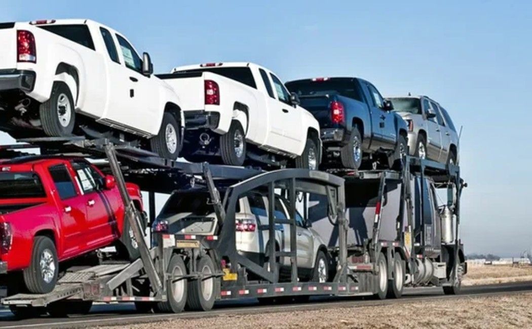 Car carrier truck loaded with red, white, and gray SUVs on a highway
