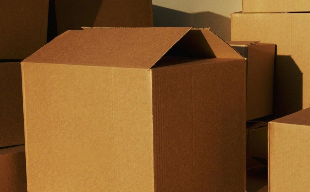 Brown cardboard moving boxes stacked in warm indoor light, one box open at the top.