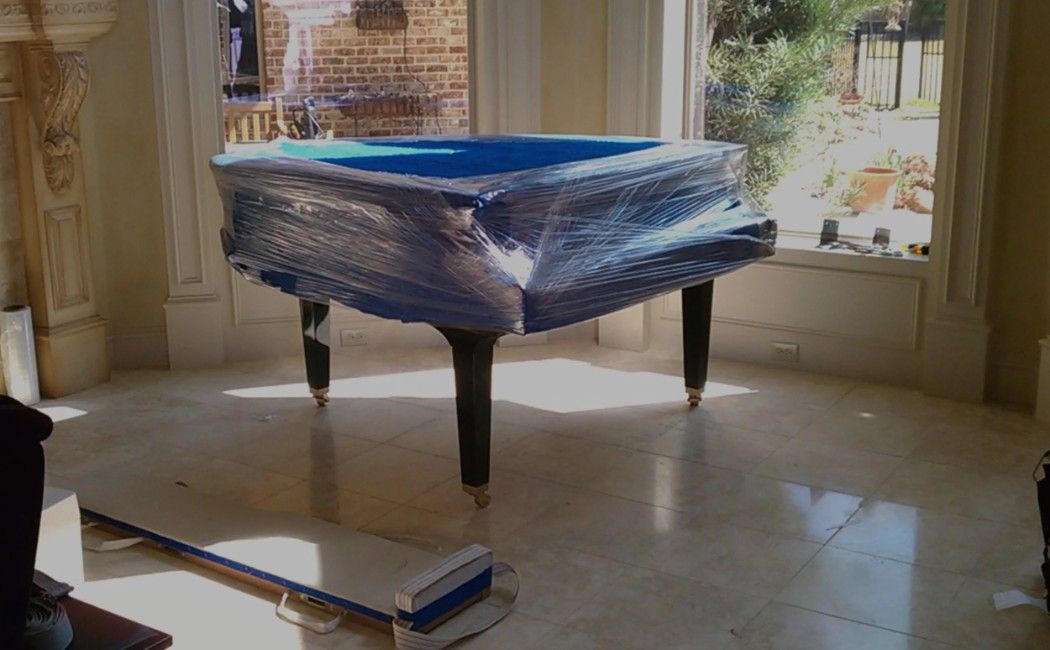 Blue pool table wrapped in plastic in a bright room, with a book on the floor nearby
