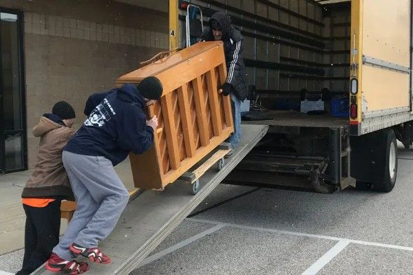 Workers loading a piano up a ramp into a truck at a warehouse loading dock