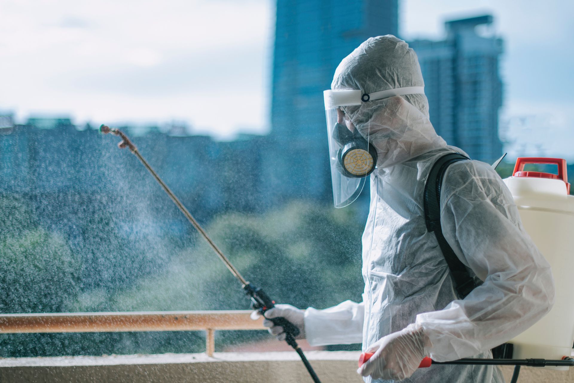 A man in a protective suit is spraying a room with pest control spray.