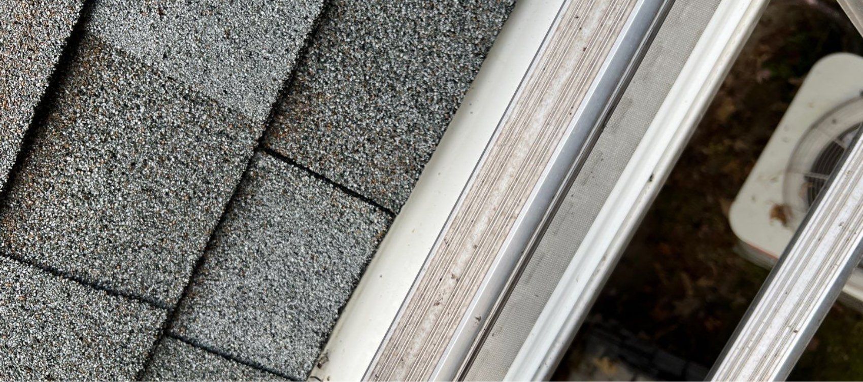 A close up of a gutter on a roof next to a window.