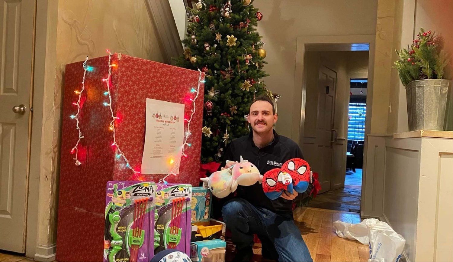 A man is sitting in front of a christmas tree holding a stuffed animal.