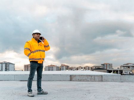 A man in a yellow jacket and hard hat is talking on a cell phone.