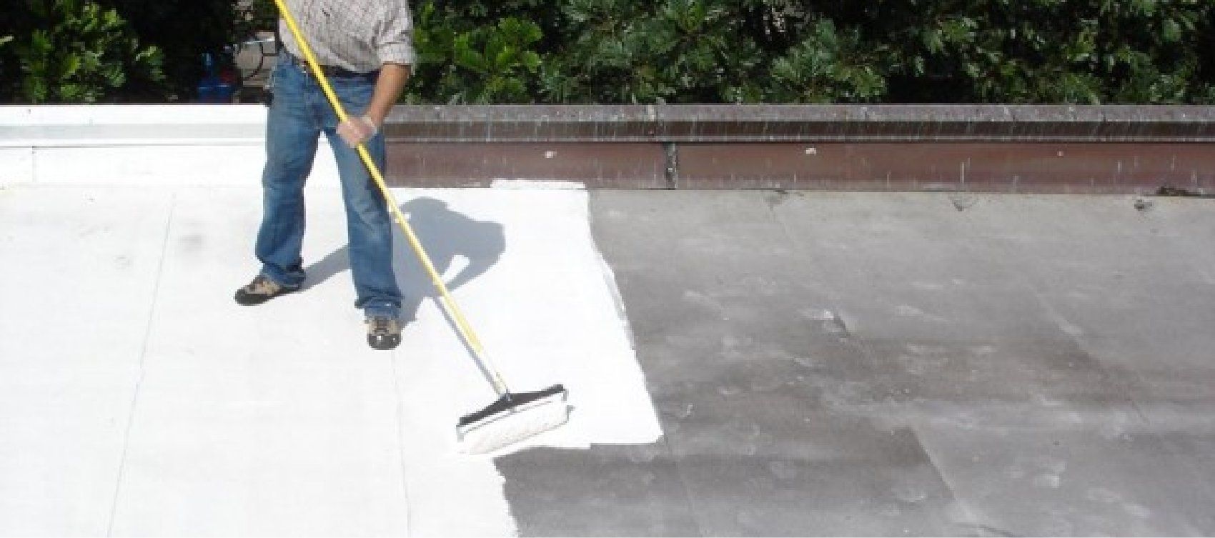 A man is painting a roof with a broom.