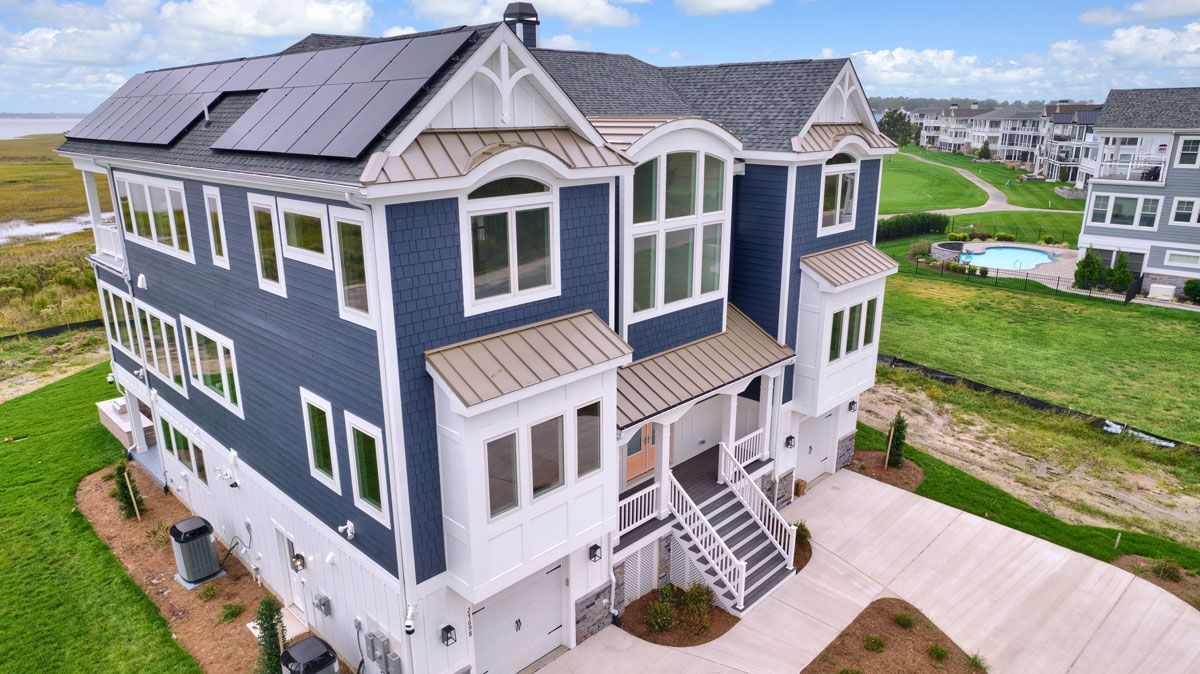 An aerial view of a large blue and white house with solar panels on the roof.