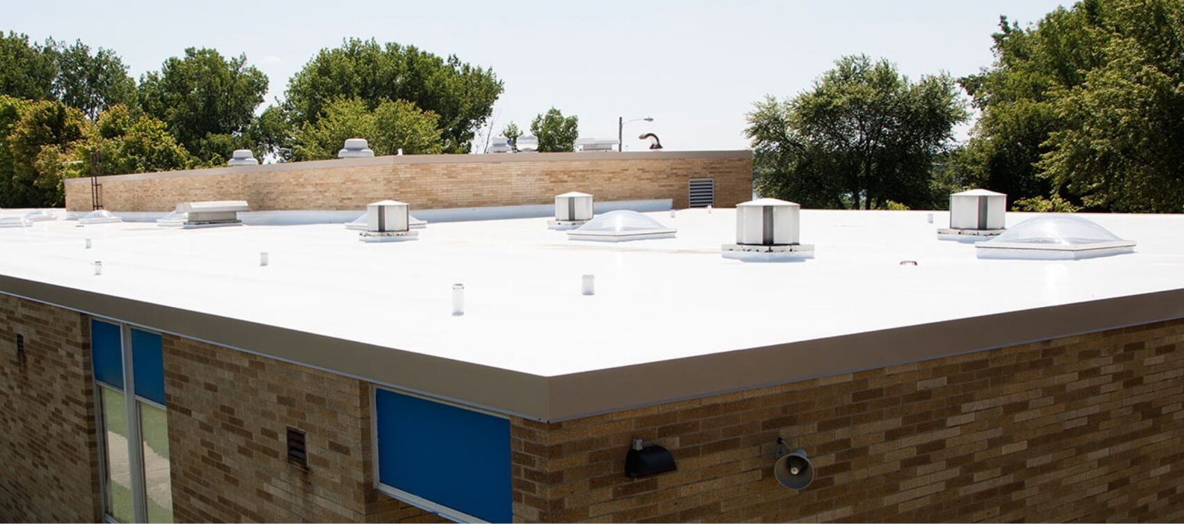 The roof of a building with a white roof and trees in the background.