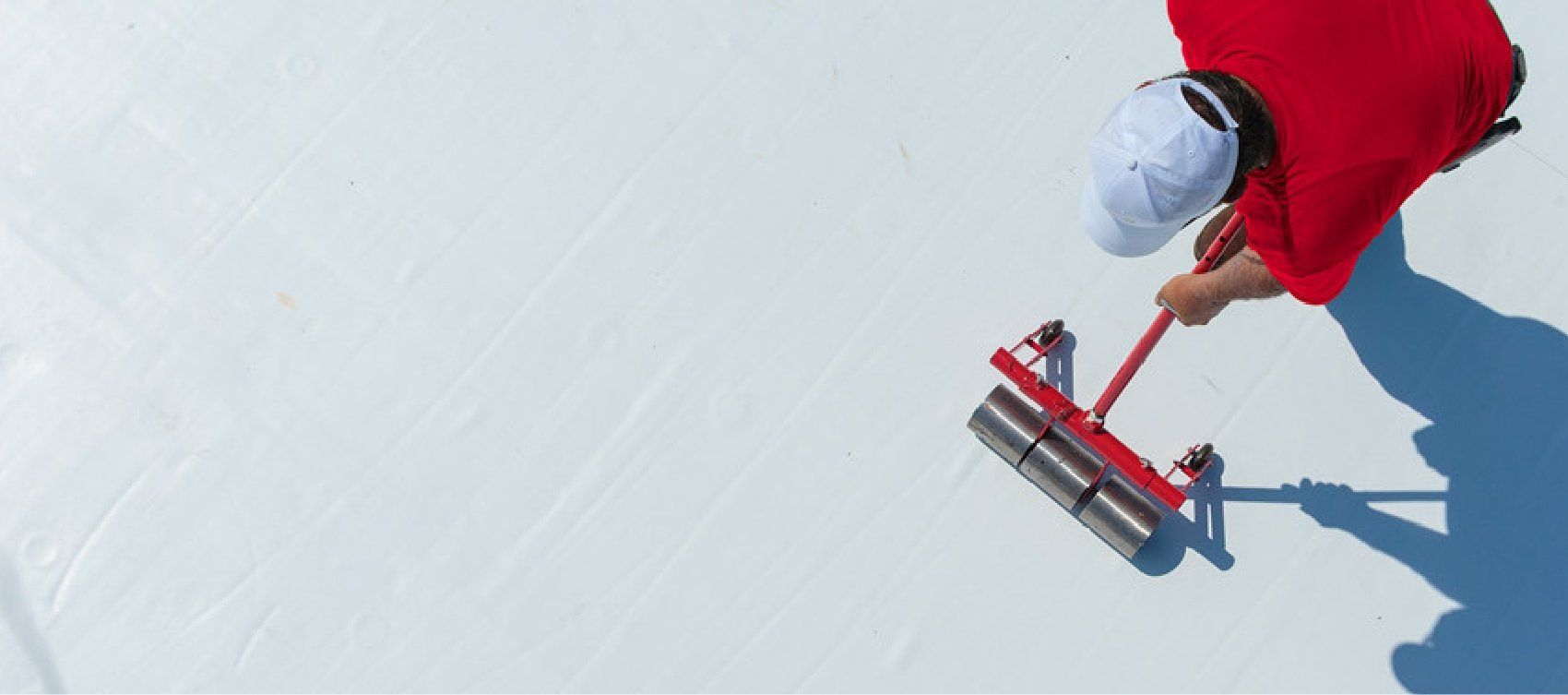 A person in a red jacket is using a broom on a white surface.