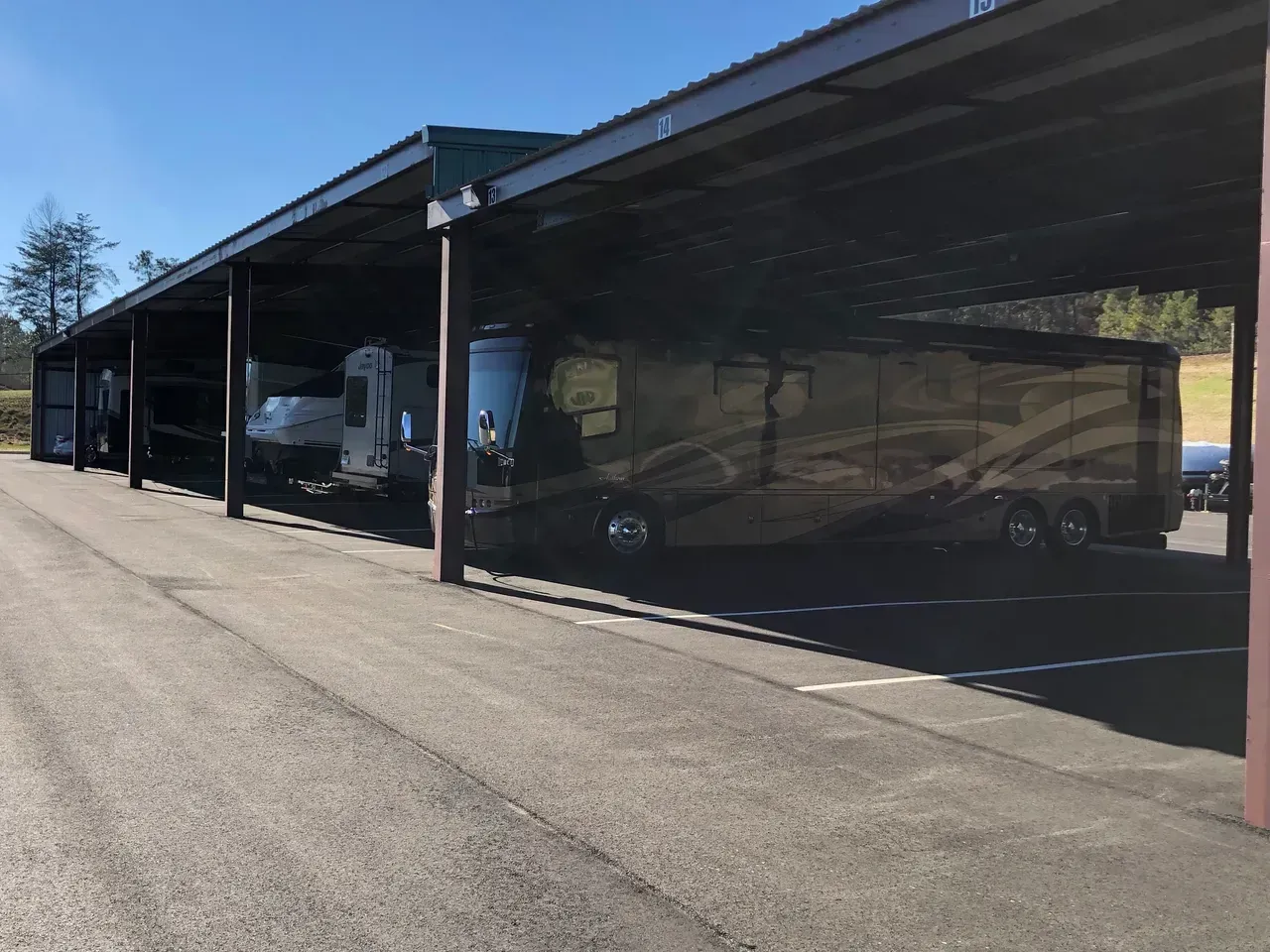 RVs parked under a covered structure on a paved lot, sunny day.