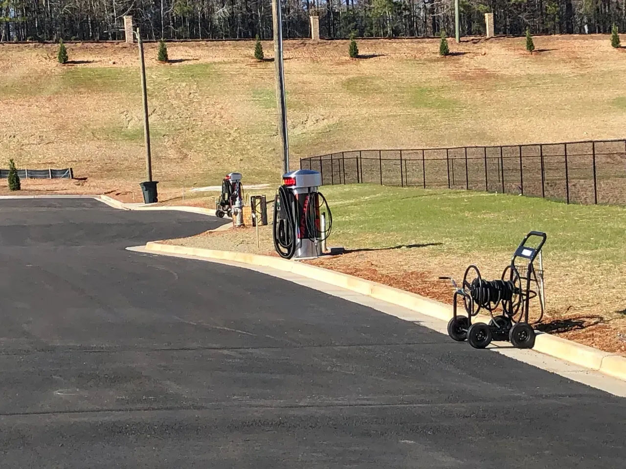 Black asphalt road with electric vehicle chargers and a utility cart along a grassy hillside.