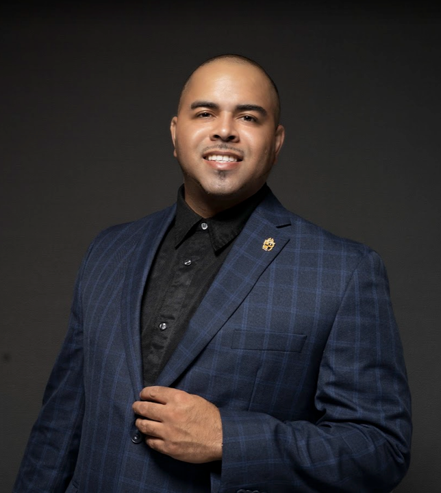 A man in a blue suit and black shirt is smiling for the camera.