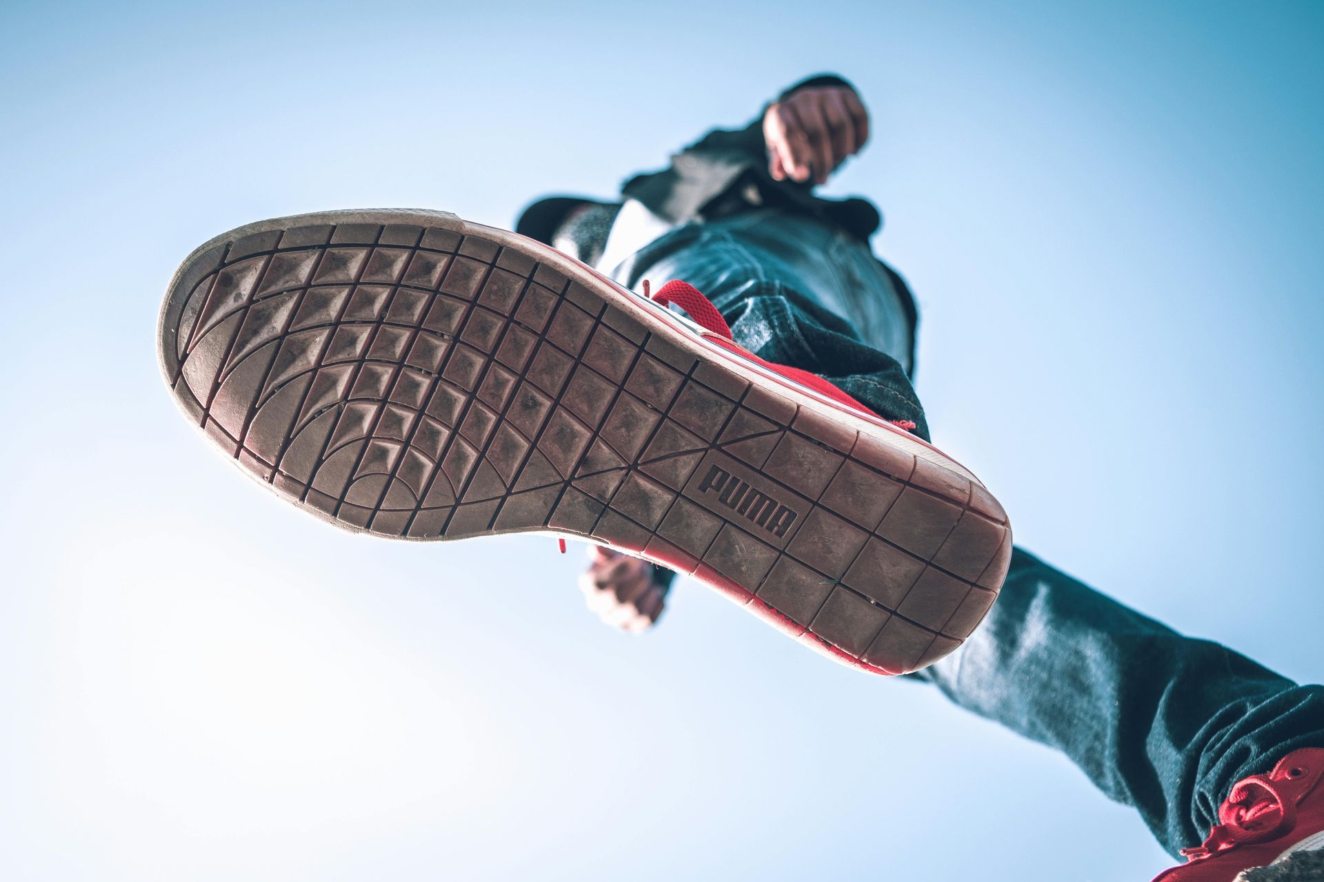 A person wearing a pair of red and white sneakers is jumping in the air.