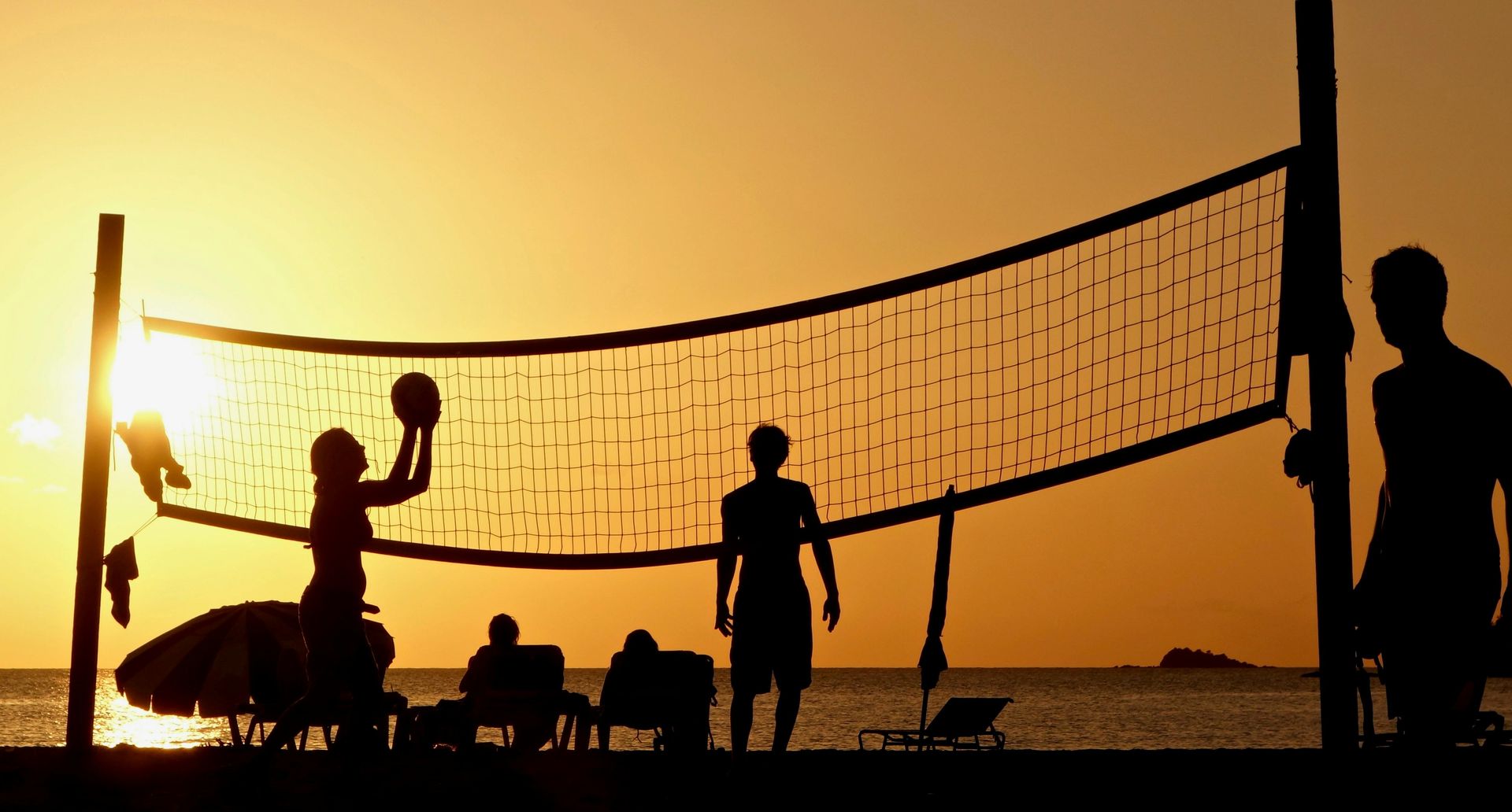 A group of people are playing volleyball on the beach at sunset